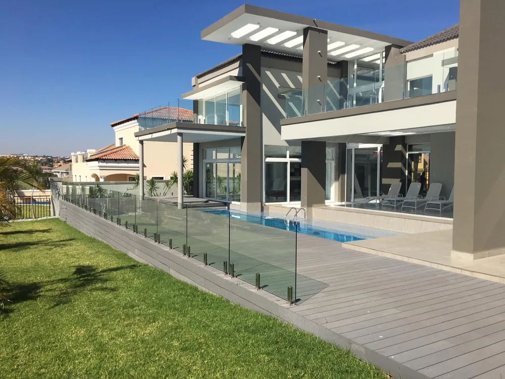 Frameless glass pool fence and grey composite deck beside a modern two-storey home with a swimming pool